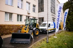 Zdjęcie stanowiska Komatsu przed budynkiem (koparka i bus serwisowy)