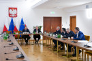 Grupa mężczyzn rozmawiających przy stole na tle flag Polski i Unii Europejskiej.