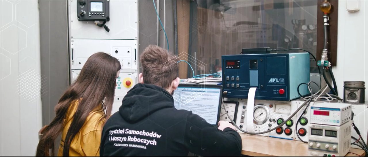 Sylwetki dwóch osób siedzących przy stole z aparaturą elektroniczną