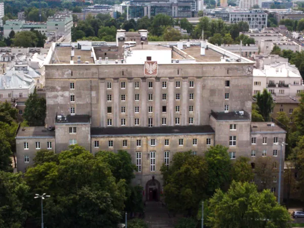 Duży gmach z godłem otoczony zielenią.