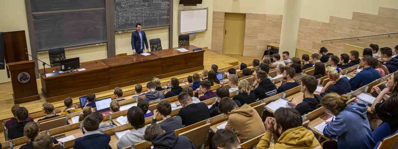 Sala audytoryjna wypełniona studentami, za katedrą stoi wykładowca.