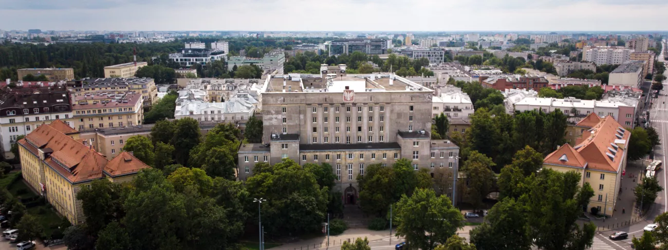 Duży gmach z godłem otoczony zielenią.