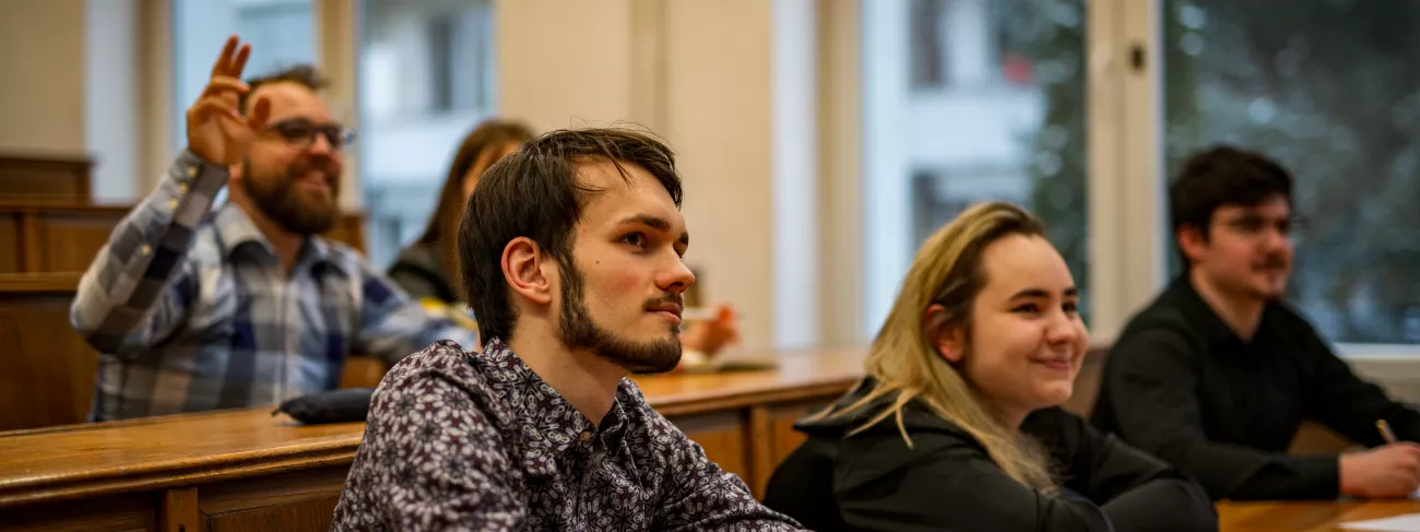 Grupa uśmiechniętych studentów w ławkach sali wykładowej.