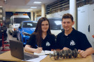 Student i studentka siedzący za stołem na tle samochodów